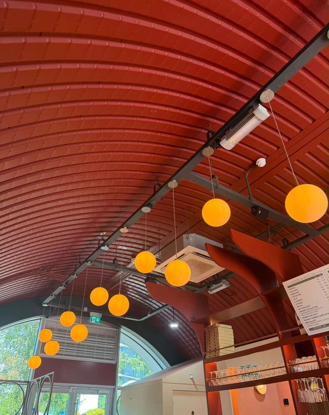 Orange globe pendants hung from a track under a curved timber ceiling in a café