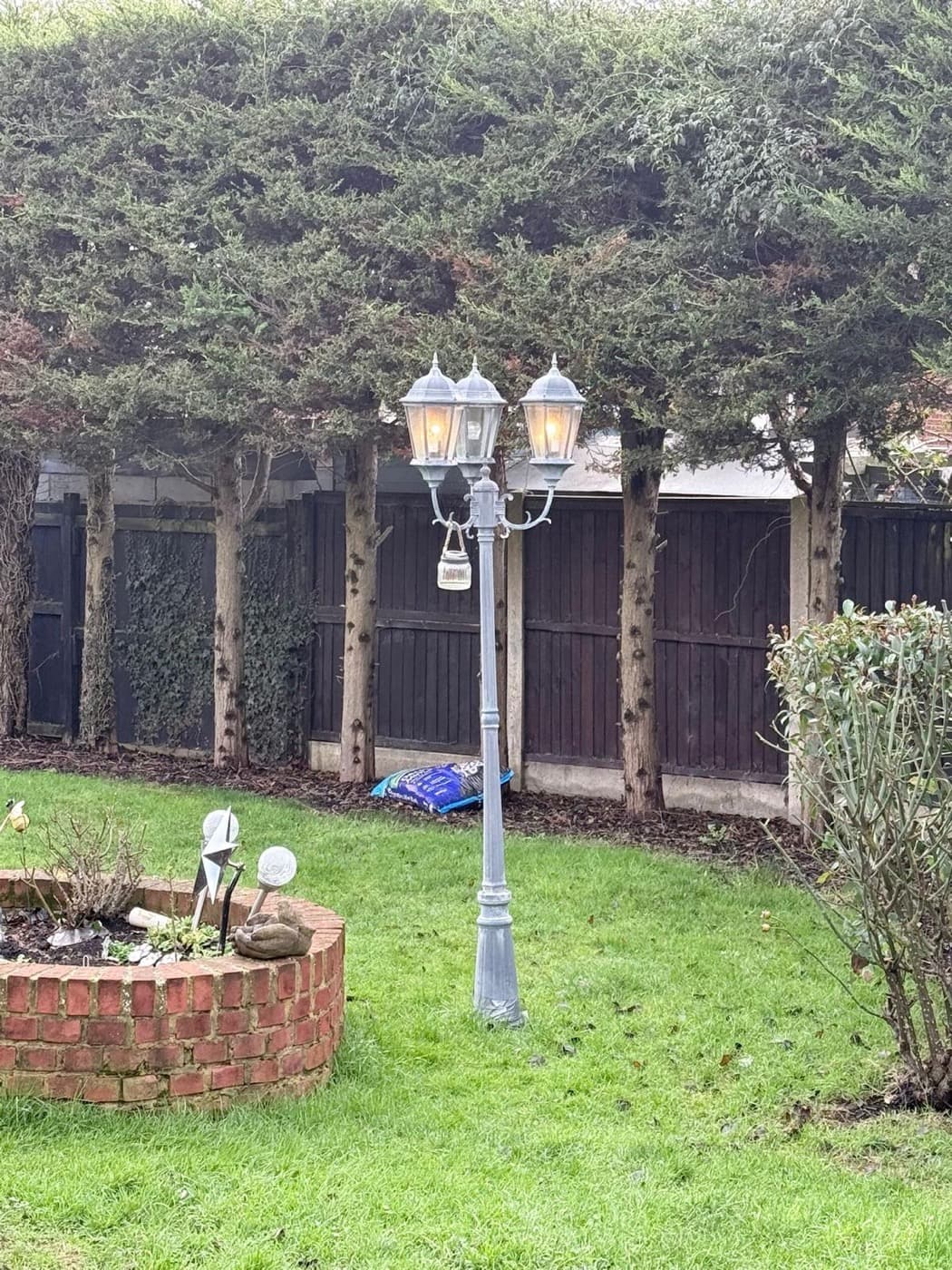 Twin-lantern lamp post fitted and lit in a garden