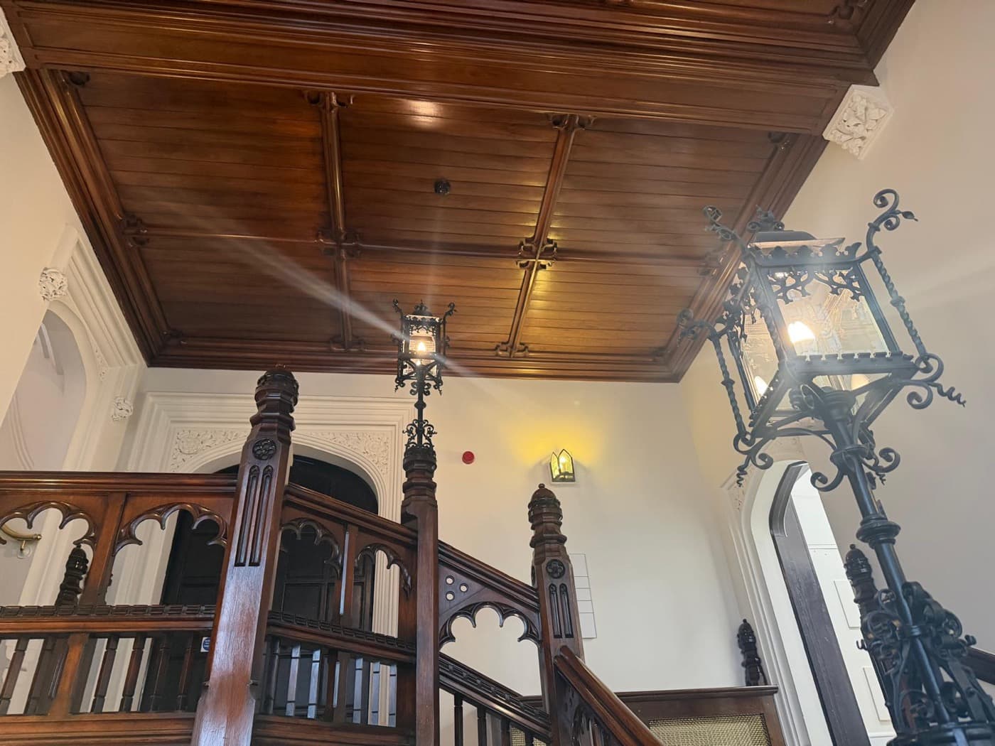 Wrought-iron lanterns fitted to a panelled timber ceiling above a period staircase