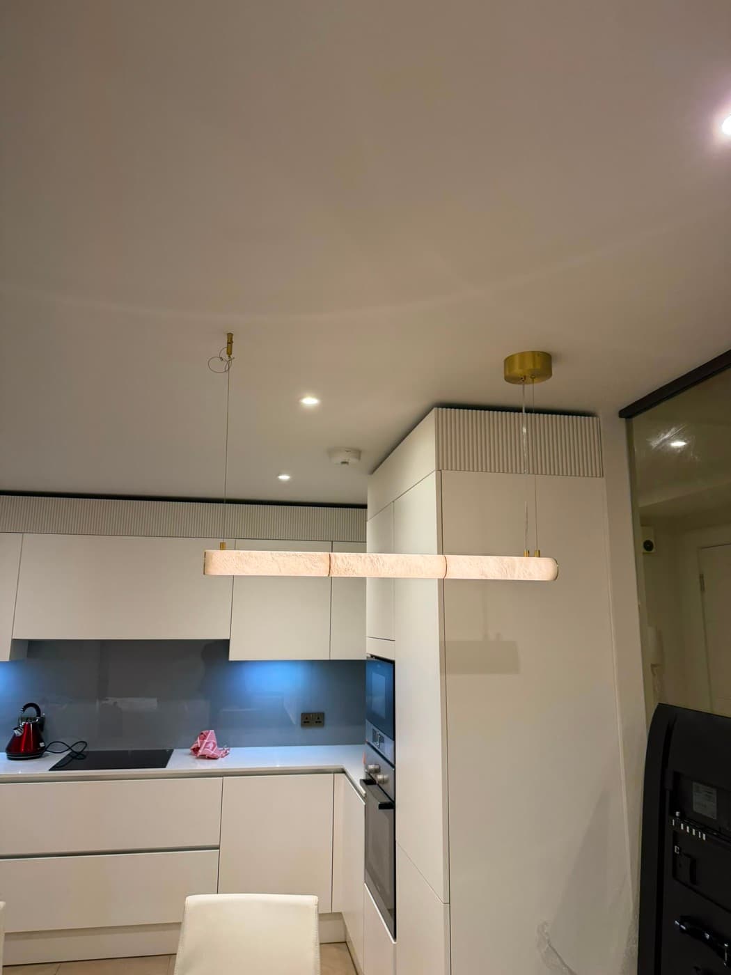 Linear pendant light over a handleless white kitchen, with downlights and lit splashback