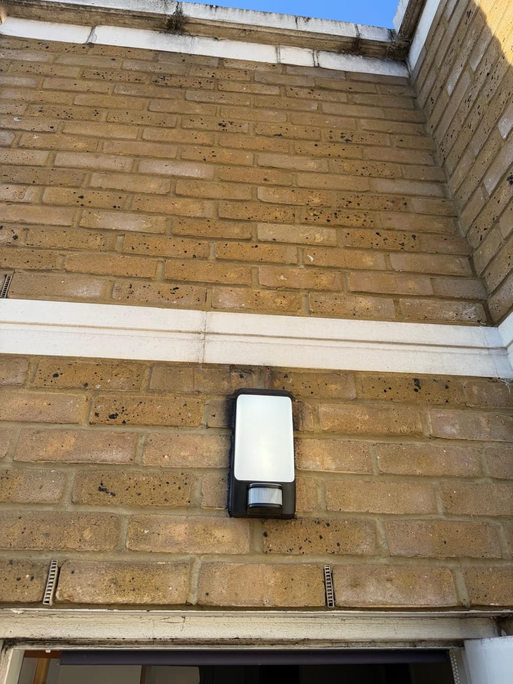 PIR security light fitted to a brick wall above a doorway